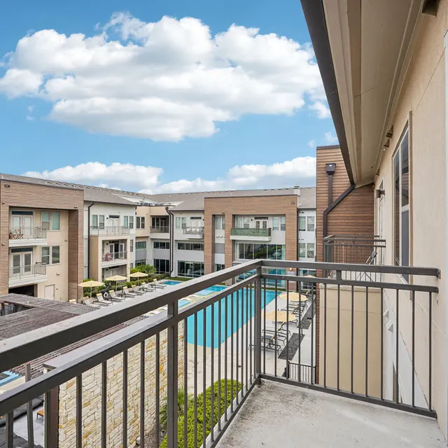View from a balcony overlooking an apartment complex with a swimming pool and landscaped grounds.