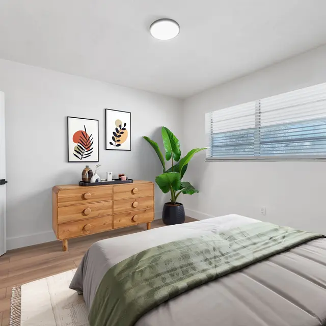 A bright and modern bedroom featuring a wooden dresser, decorative plants, and wall art.