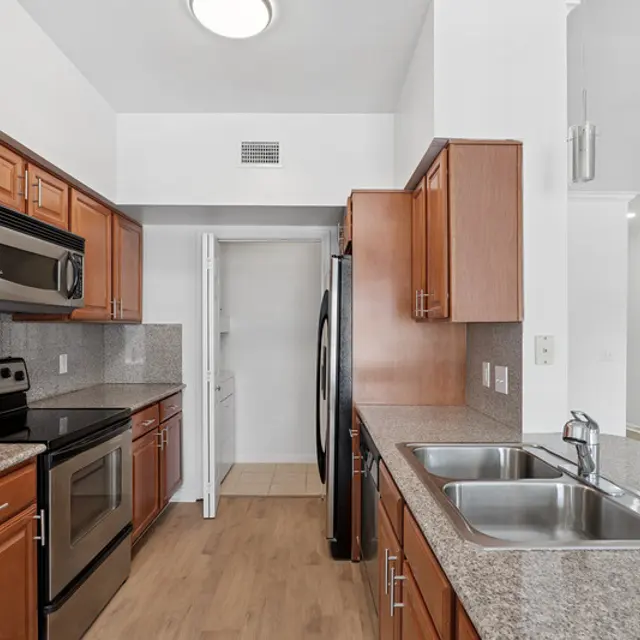 A modern kitchen featuring wooden cabinets, stainless steel appliances, and a granite countertop with double sinks.