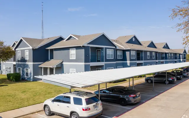 A view of an apartment complex with two-story buildings and a carport in the foreground.