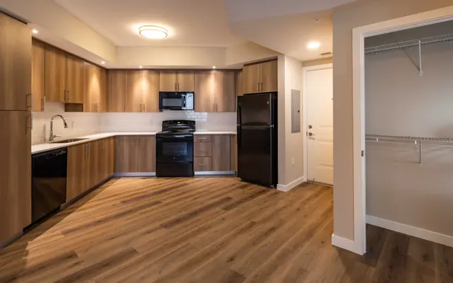 A modern kitchen featuring wooden cabinetry, black appliances, and a light-colored countertop with an open layout.