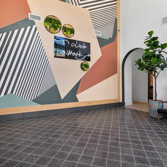Modern Clubhouse Entryway A modern clubhouse entryway featuring a colorful geometric mural on the wall and a stylish black seating area with a small potted plant.