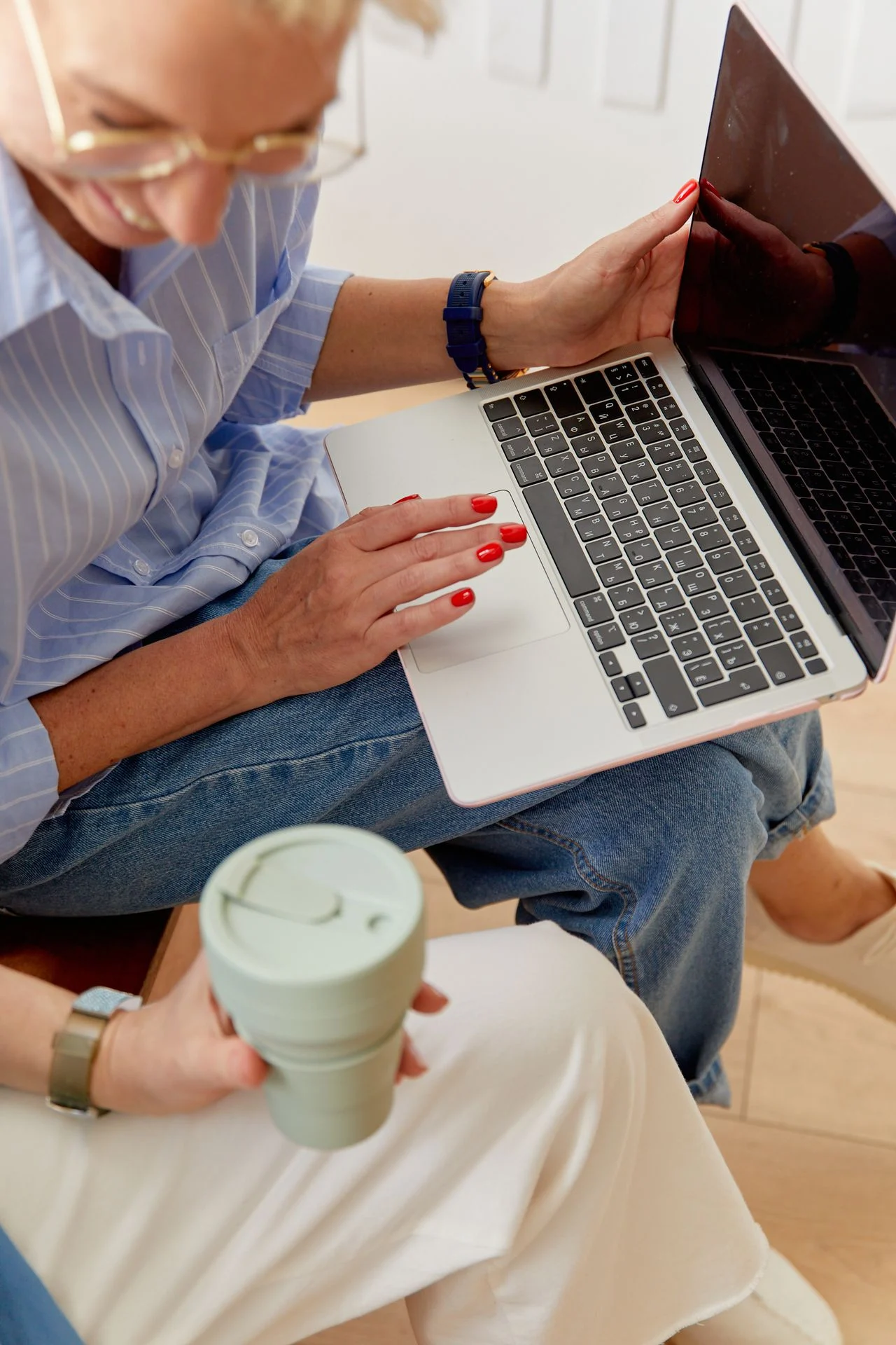 Two women sitting together, one using a laptop and the other holding a reusable coffee cup.