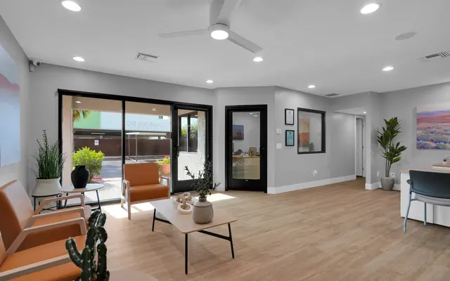 A modern waiting area featuring stylish furniture and decor, including orange chairs, a coffee table, and potted plants.