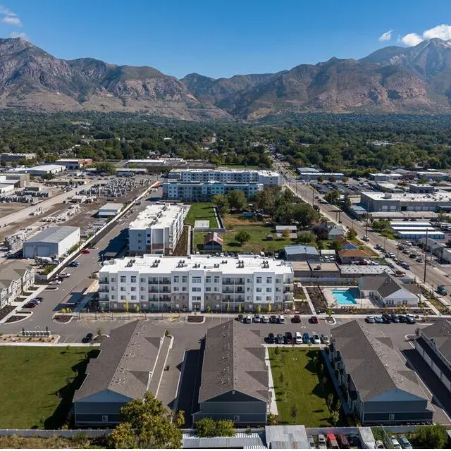 An aerial view of a residential area surrounded by mountains, featuring several buildings, parking lots, and green spaces.