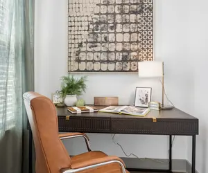 Cozy Home Office Corner A cozy home office corner featuring a dark wooden desk with a modern lamp and decorative items, a stylish chair, and a piece of abstract wall art.