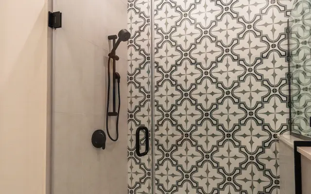 A modern shower with a glass enclosure, featuring a patterned tile wall and a rainfall shower head.