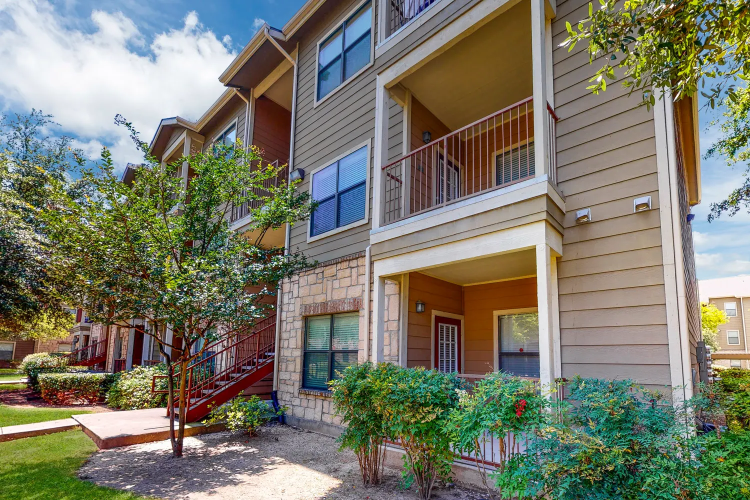 Multi-Story Apartment Complex Exterior view of a multi-story apartment building with light green and beige siding, surrounded by greenery and trees.