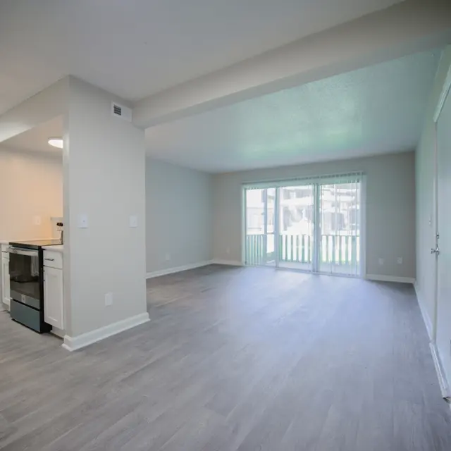 Spacious living room area with light-colored walls and flooring, featuring a view of an outdoor patio through sliding glass doors.