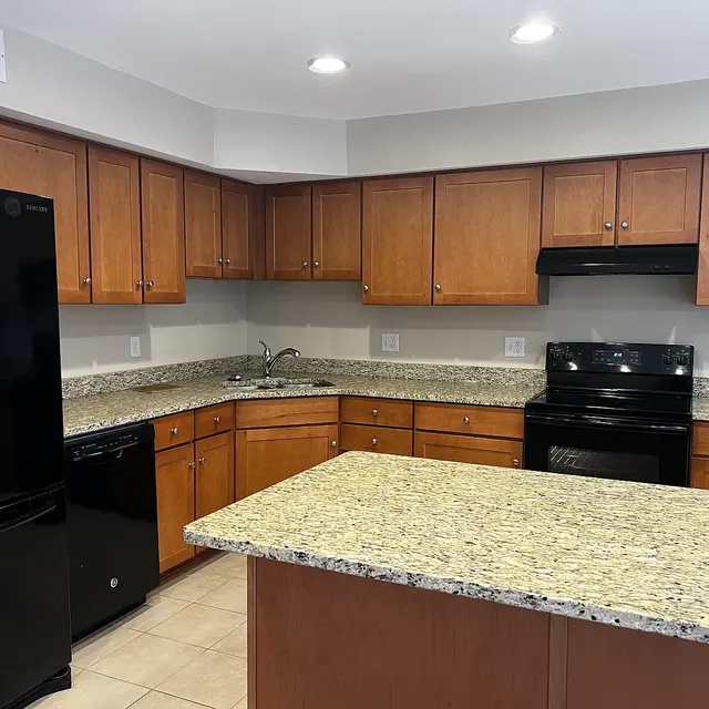 A modern kitchen featuring wooden cabinetry, granite countertops, and black appliances including a refrigerator and stove.