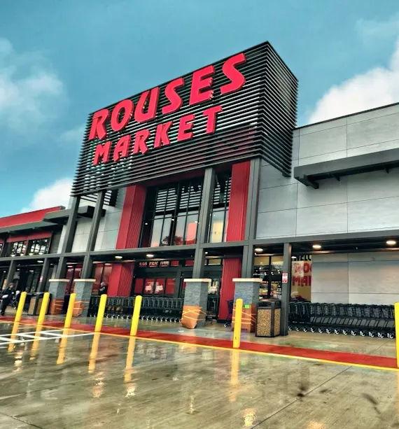 Exterior of Rouses Market building with a bright sign and wet pavement.