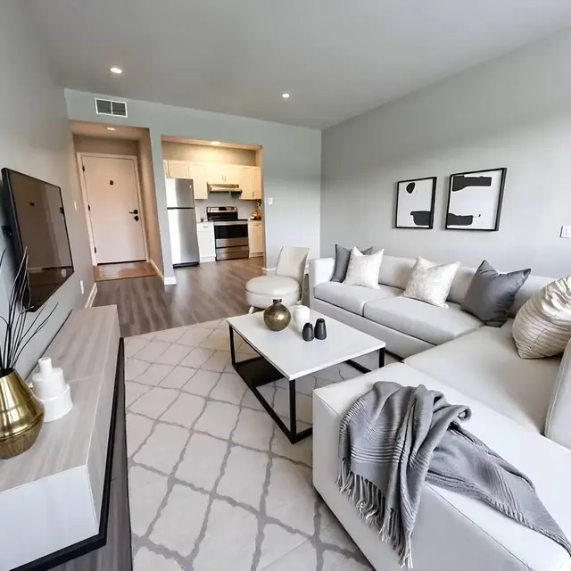 Modern living room with a gray sofa, coffee table, minimalist decor, and a view of a kitchen area in the background.