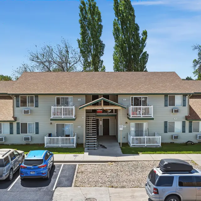 Aerial View of Apartment Complex Aerial view of a two-story apartment complex featuring a central entrance and outdoor stairway, surrounded by green grass and several parked cars.