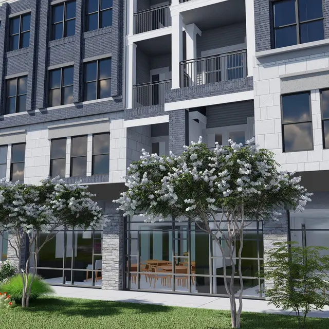 A modern apartment building with a mix of brick and stone exterior, featuring large windows and a landscaped area in front with trees and flowerbeds.