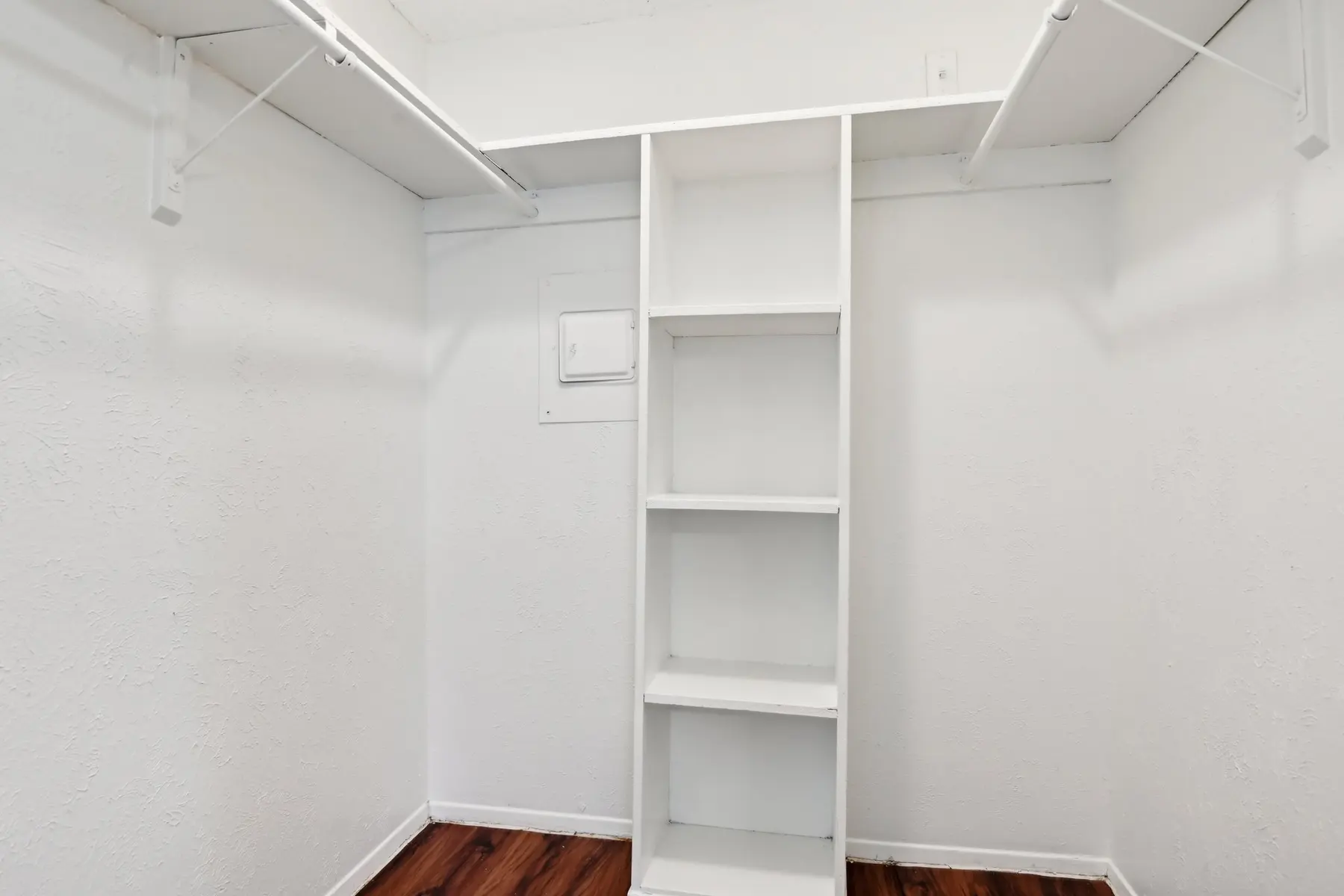 An empty closet with white walls and built-in wooden shelving.
