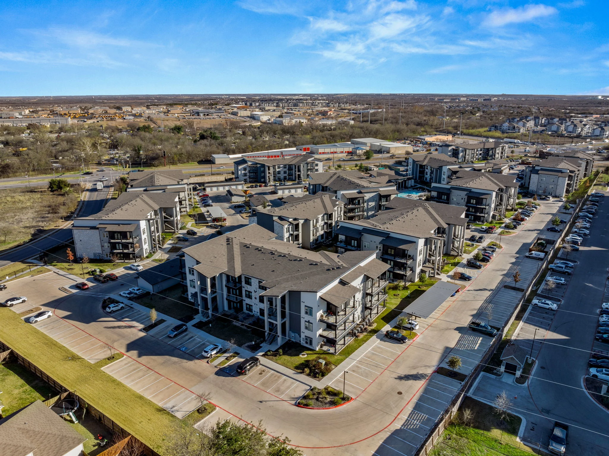 Aerial view of a modern apartment complex featuring multiple buildings, parking spaces, and green areas.