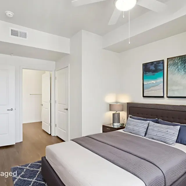 Stylish Modern Bedroom A modern bedroom featuring a bed with gray bedding, two side tables with lamps, and two framed artworks on the wall. The room has a ceiling fan and a large closet visible in the background.