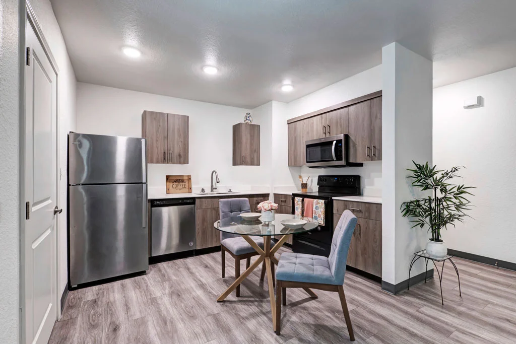 A modern kitchen featuring stainless steel appliances, wooden cabinetry, and a small dining table with two chairs in a well-lit space.