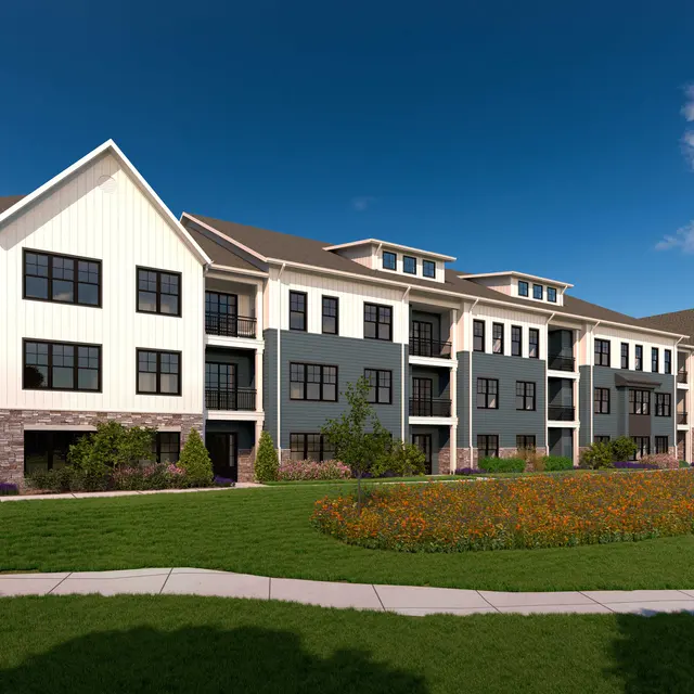 A modern apartment complex featuring a combination of white and gray exterior finishes, surrounded by green lawn and colorful flower beds under a clear blue sky.