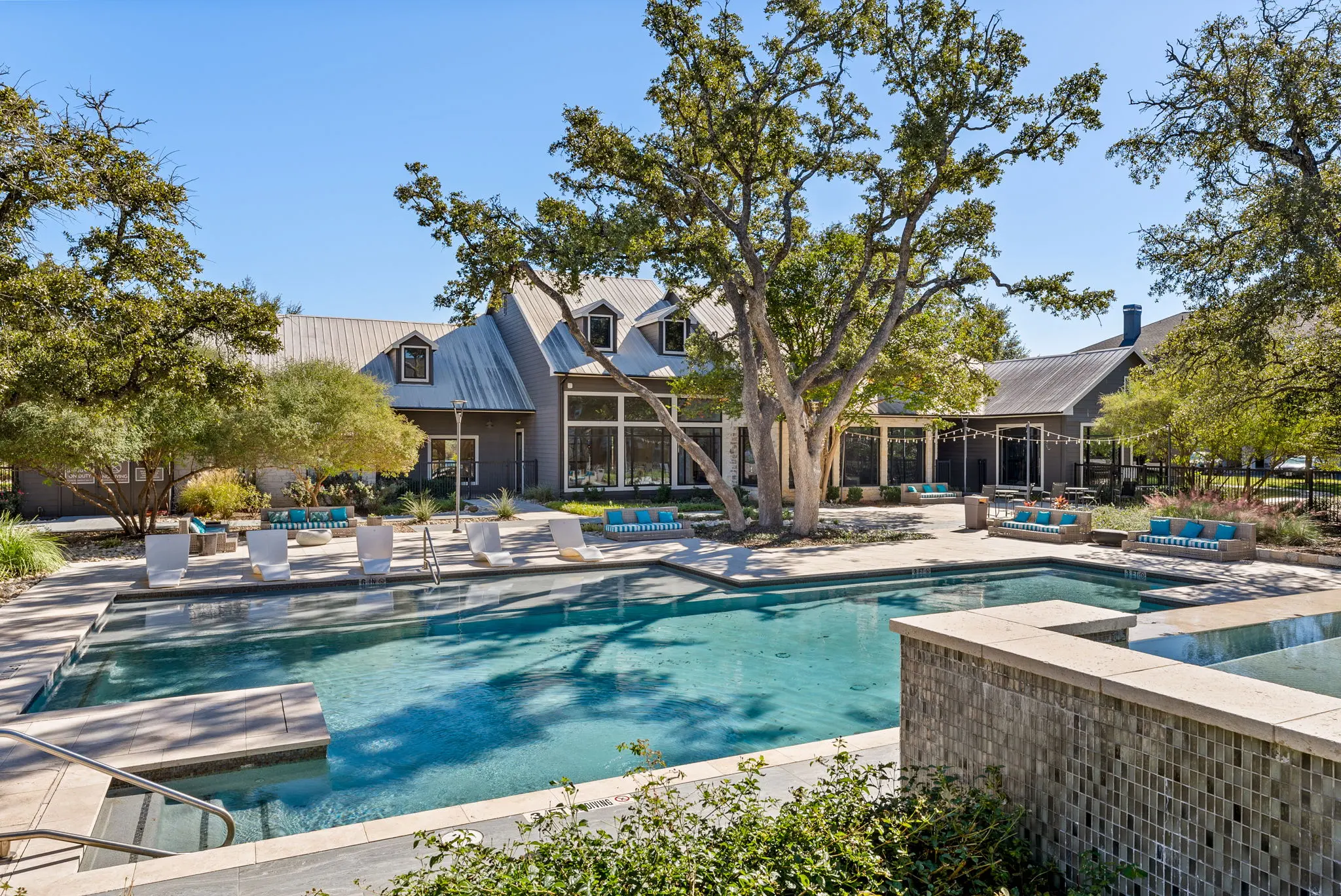 A luxurious outdoor pool area with lounge chairs surrounding a sparkling pool, nestled among trees and a modern building in the background.