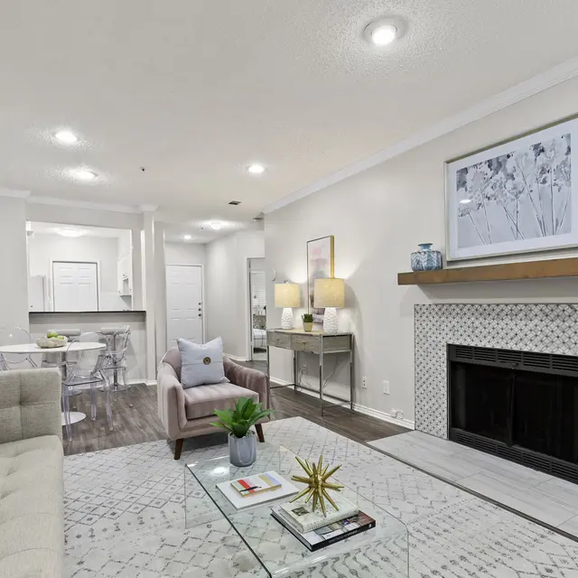 Modern Living Room Interior A modern living room featuring a beige couch, a glass coffee table, and a fireplace with decorative tiles. The space includes a dining area and has neutral-colored walls with a framed artwork.