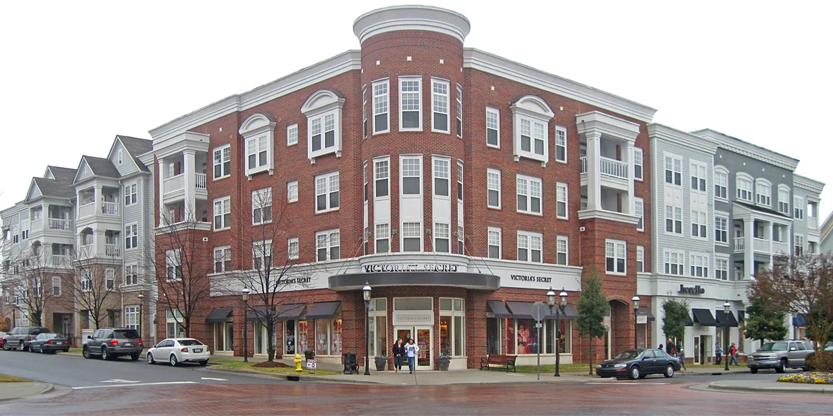An urban building with a brick facade and multiple stories, featuring large windows and balconies, surrounded by other structures and parked cars.