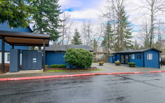A view of two blue buildings in a parking lot, with green bushes and trees.