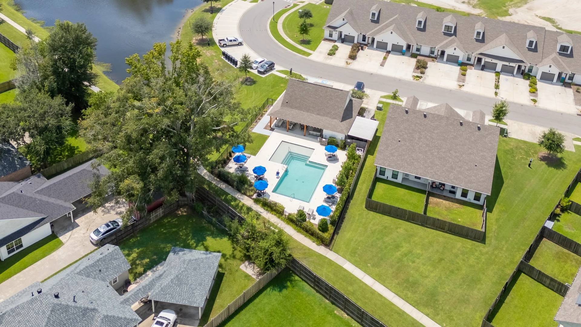 Aerial view of a neighborhood featuring a swimming pool, surrounding houses, and a pond.
