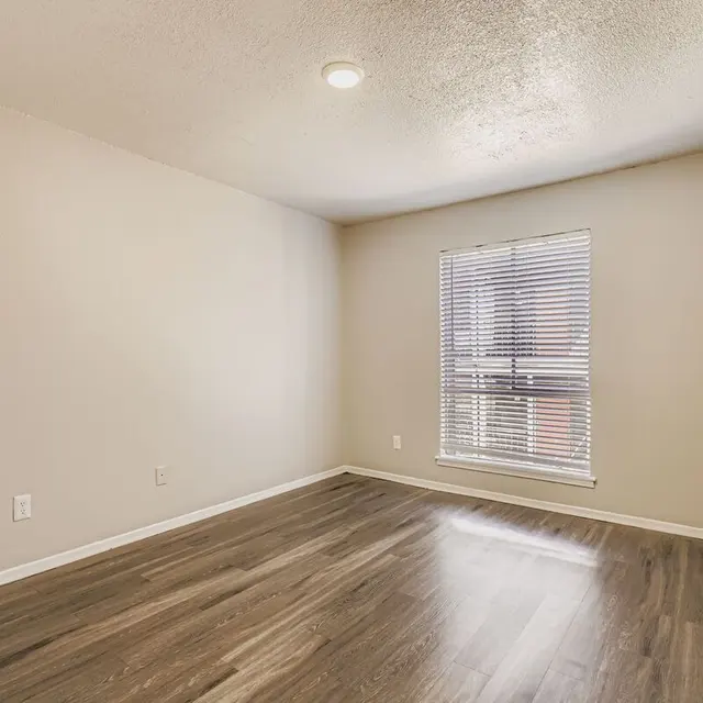 A vacant room featuring a window with blinds, light-colored walls, and dark wood flooring.