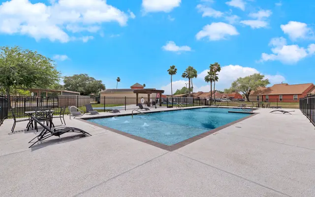 Swimming Pool at Apartment Complex A clean, inviting swimming pool area surrounded by lounge chairs and palm trees, set against a blue sky with fluffy white clouds.