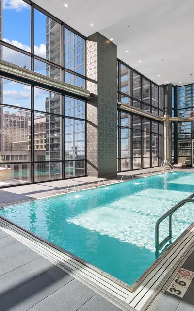 A modern indoor pool area featuring large windows that allow natural light to fill the space, surrounded by tall buildings.