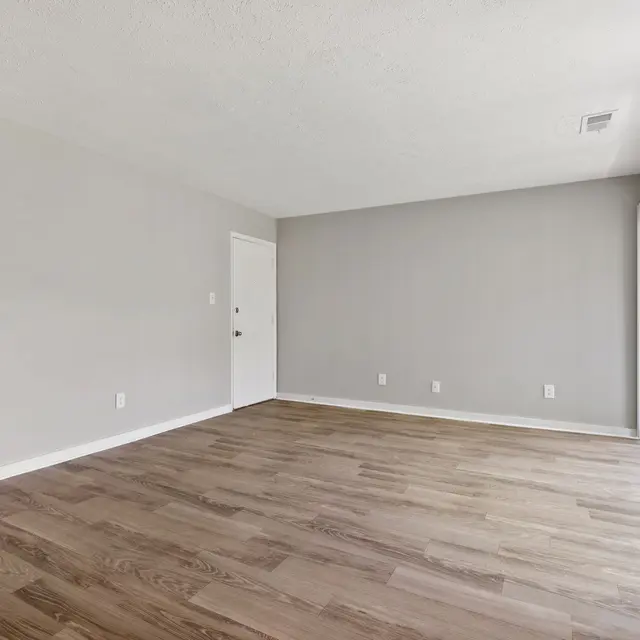 Empty room with light grey walls, wood flooring, and large sliding glass doors. A door is visible on the left side.