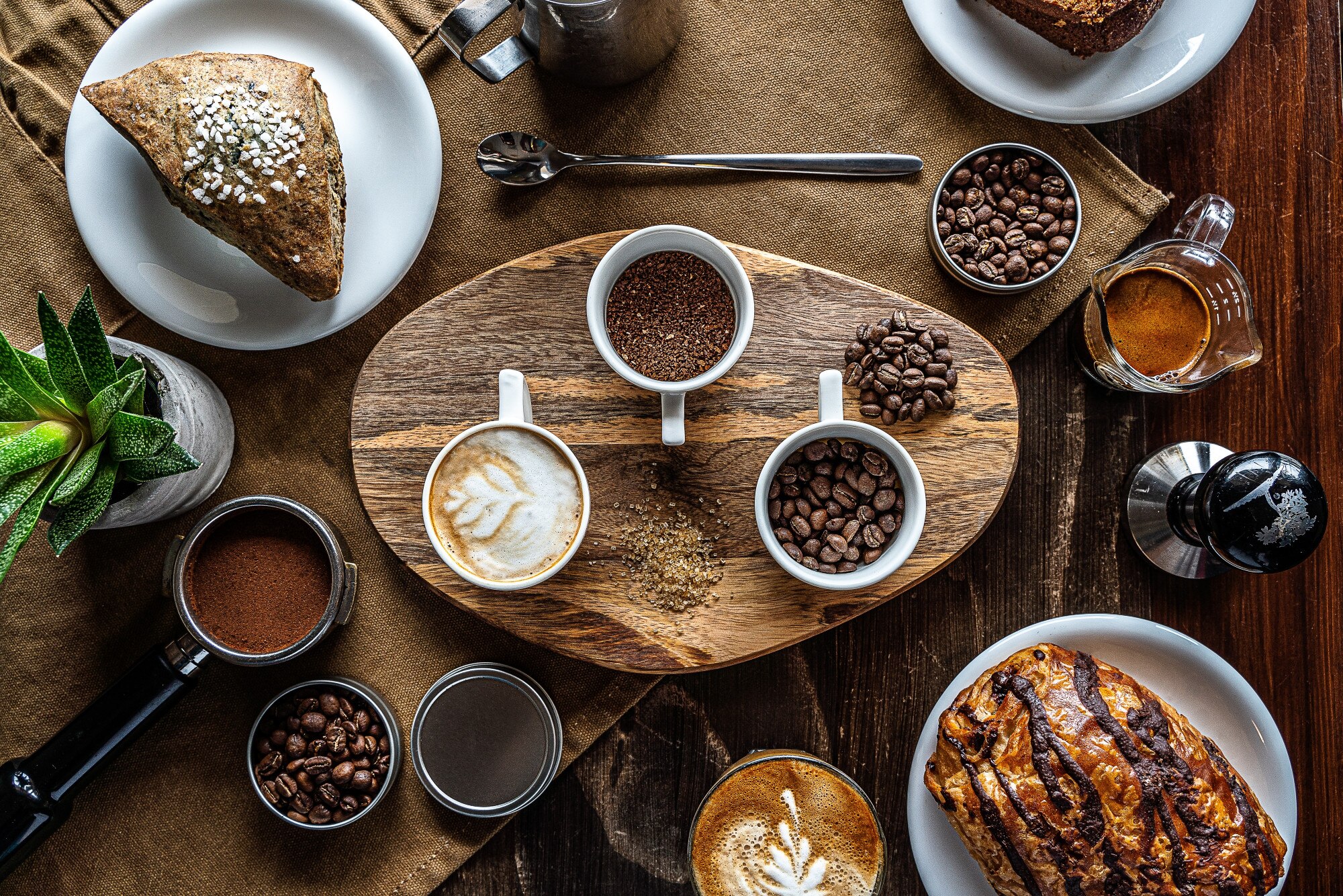 A flat lay of a breakfast spread featuring coffee, pastries, and coffee beans on a wooden table.