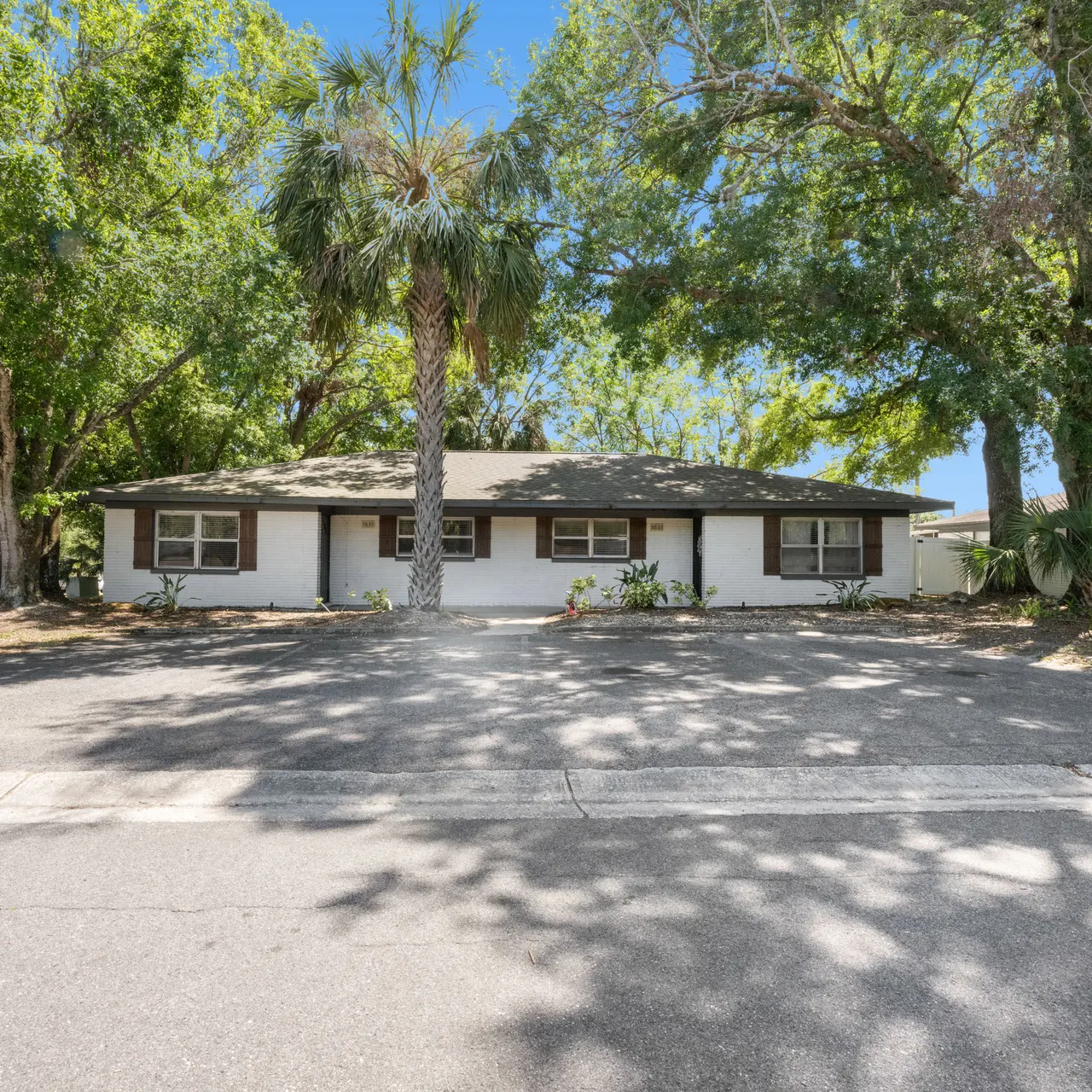 A single-story house surrounded by trees, showing a lush front yard with pavement leading to it.