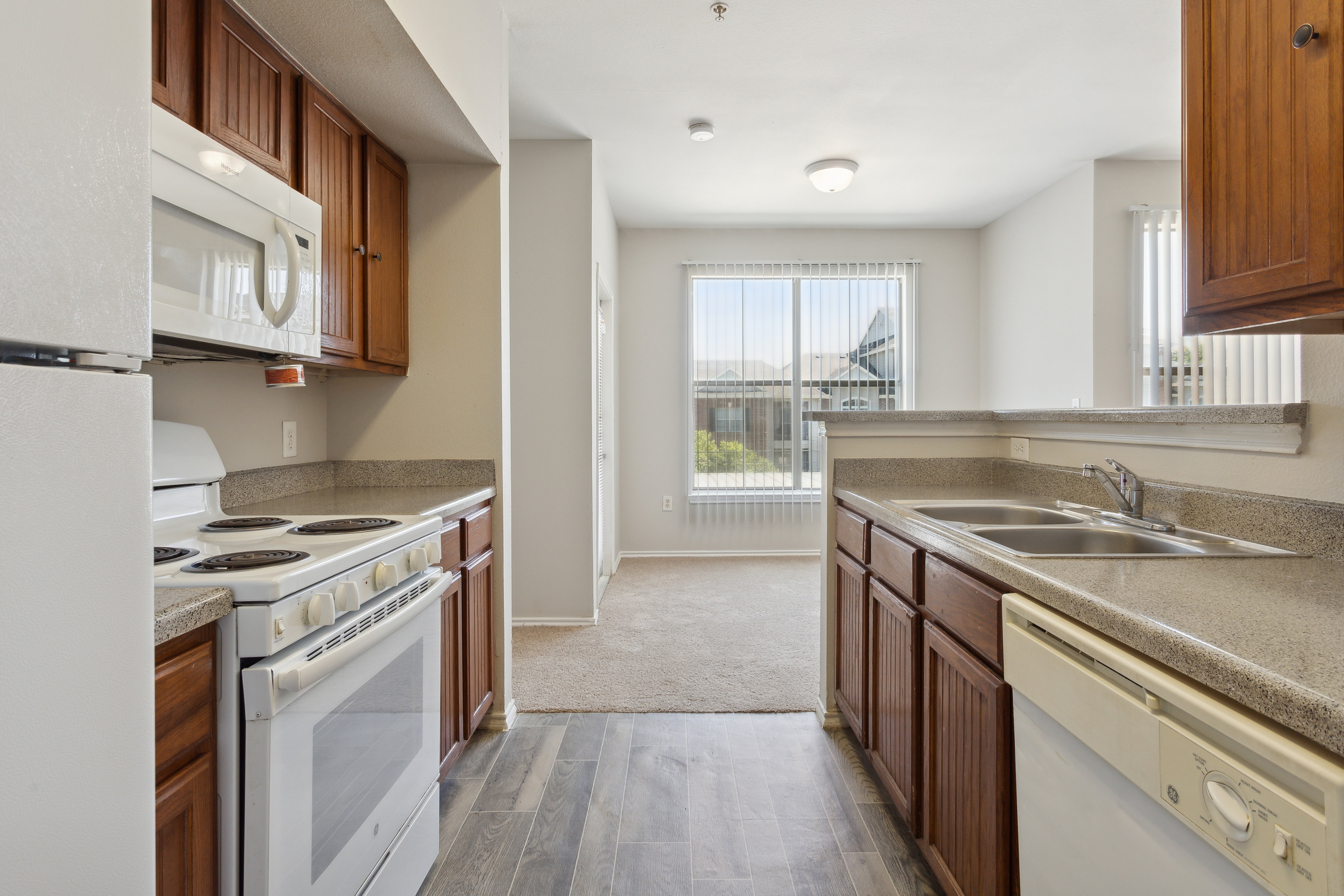 Modern Kitchen Interior A view of a modern kitchen with wooden cabinetry and granite countertops. The kitchen features a stove, microwave, and dishwasher with a view of a well-lit living area.
