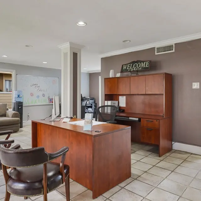 A welcoming reception area featuring a desk with a chair, two armchairs, a couch in the background, and large glass doors leading to an outdoor pool area.