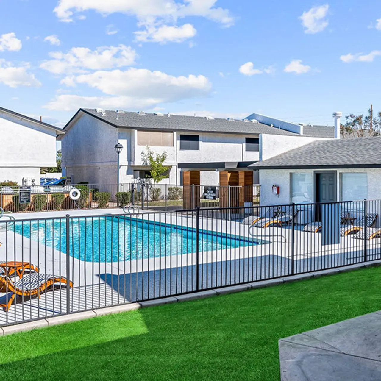 Outdoor pool area surrounded by a fence with lounge chairs