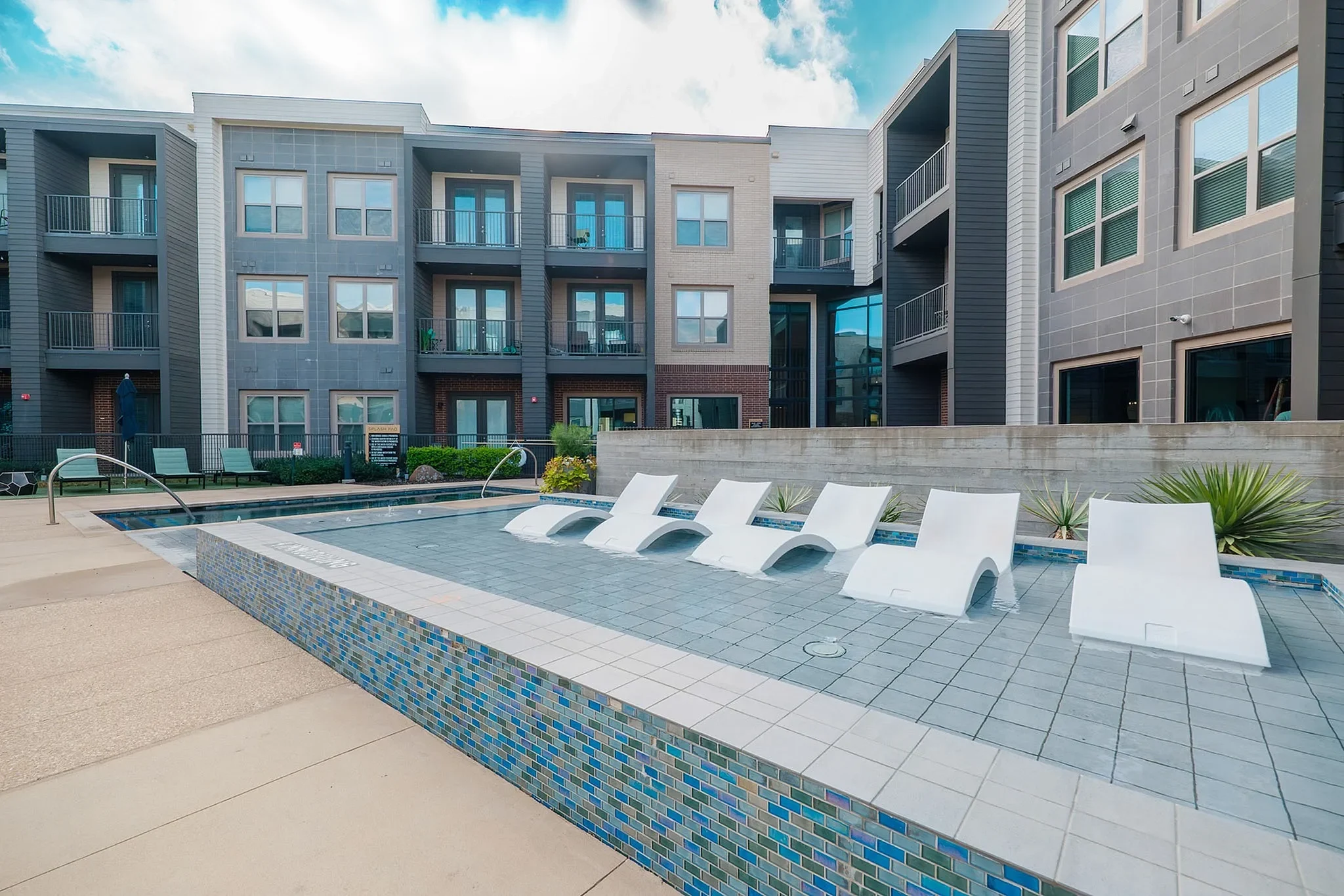 Modern Apartment Pool Area The view of a modern apartment complex with a swimming pool area featuring white lounge chairs and surrounded by greenery.
