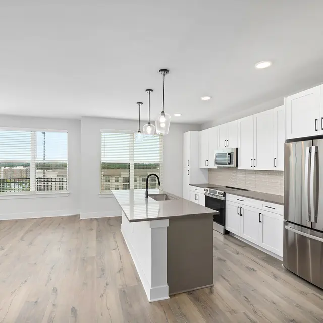 Modern Kitchen Interior A modern kitchen featuring white cabinets, a stainless steel refrigerator, an island with a gray countertop, and large windows letting in natural light.