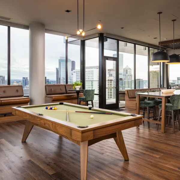 A modern game room featuring a pool table, green chairs, and large windows showcasing a city skyline.