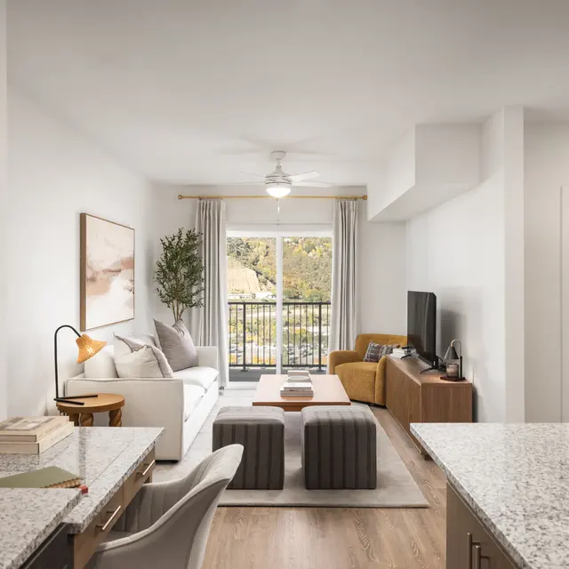 A modern living room with a neutral color palette, featuring a sofa, yellow armchair, coffee table, and a balcony view. The space has wooden flooring and an open layout.