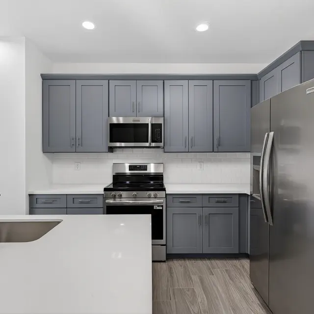 A modern kitchen featuring gray cabinets, stainless steel appliances, and a large island with a sink.