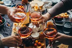 A group of four people toasting with glasses of rosé wine over a table spread with cheese, fruits, and snacks.