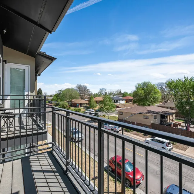 View from a balcony overlooking a residential neighborhood with houses and vehicles on the street under a clear blue sky.