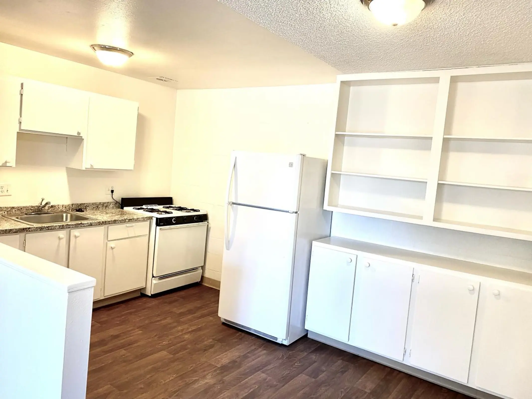 Kitchen with white cabinets, stove, refrigerator and open shelving.