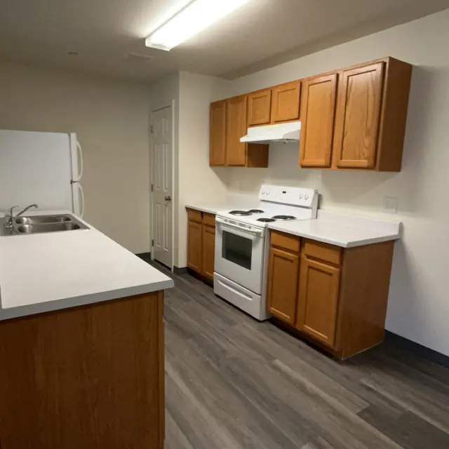A modern kitchen space featuring wooden cabinets, a white stove, and a sink on a white countertop with gray flooring.