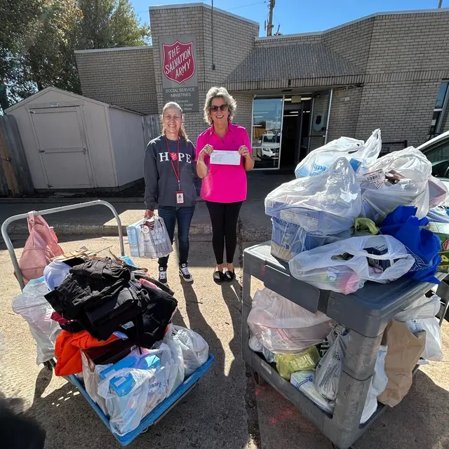 Two women standing outside a Salvation Army building, one holding a donation receipt, surrounded by bags of donated clothing.