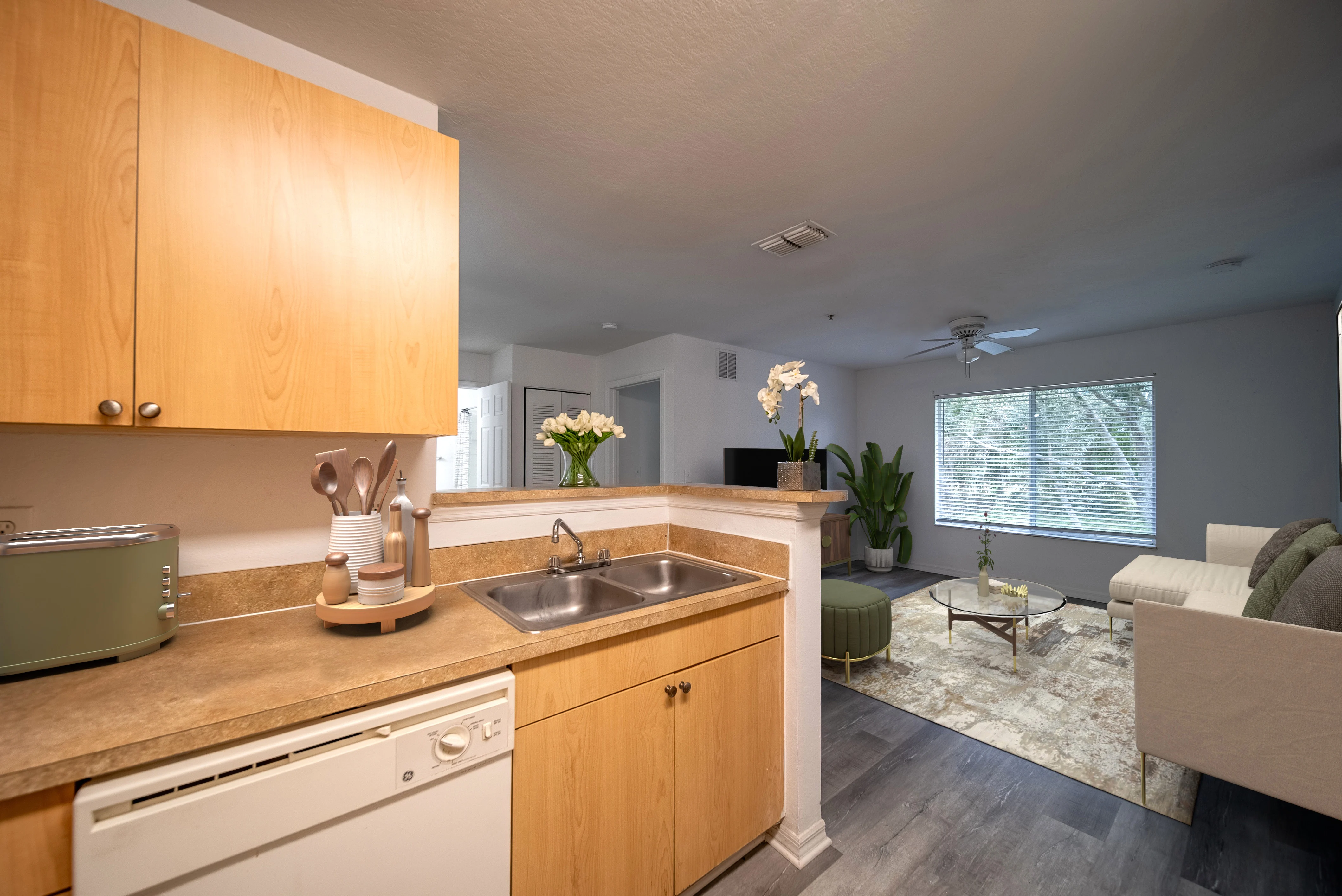 A modern apartment featuring a kitchen with wooden cabinets and a living room with a sofa and large window.