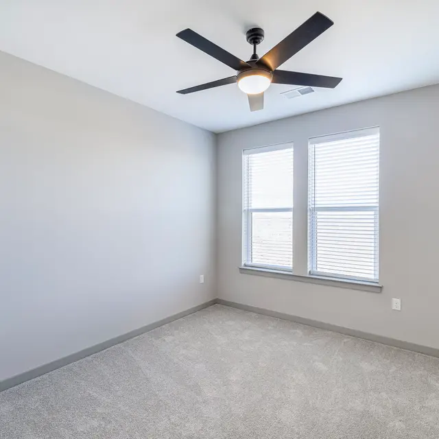 Empty Bedroom with Ceiling Fan An empty bedroom featuring a ceiling fan with light, light gray walls, and two windows with blinds.