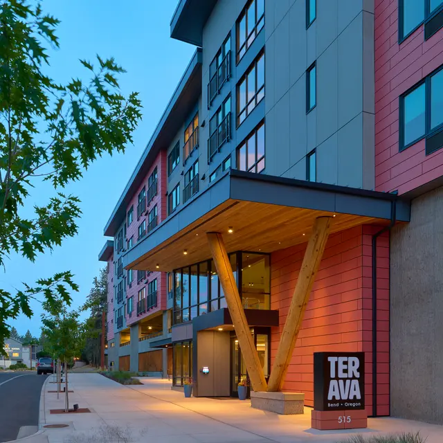 Modern multi-story building entrance with wooden accents and a prominent sign.